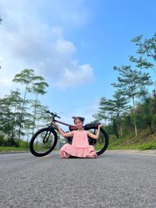 Una chica está sentada en la carretera con una bicicleta en Biệt thự hoa Xương Rồng - Venus Flamingo resort - Biệt thự trên đồi 6 phòng - BBQ, bể bơi, karraoke free, en Phúc Yên