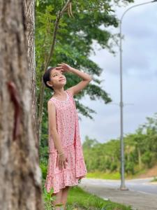 Una niña con un vestido rosa de pie junto a un árbol en Biệt thự hoa Xương Rồng - Venus Flamingo resort - Biệt thự trên đồi 6 phòng - BBQ, bể bơi, karraoke free, en Phúc Yên