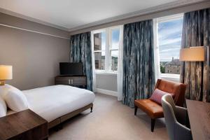 a hotel room with a bed and a chair and window at Hilton Edinburgh Carlton in Edinburgh