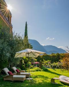 a patio with chairs and an umbrella in the grass at Hotel Gartenresidence Zea Curtis in Merano