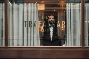 a man standing in a window with a sign on it at The Trafalgar St. James, London Curio collection by Hilton in London