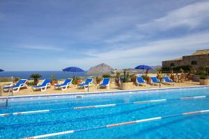 a swimming pool with chairs and umbrellas and the ocean at Hotel Baglio Santacroce in Valderice