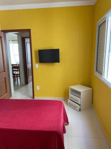 a bedroom with a bed and a tv on a yellow wall at Apartamento Ubatuba Toninhas in Ubatuba