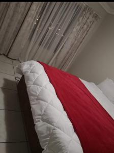 a bed with a red and white blanket next to a window at Sagewood Manor in Midrand