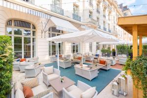 an outdoor patio with white chairs and tables and umbrellas at Waldorf Astoria Versailles - Trianon Palace in Versailles