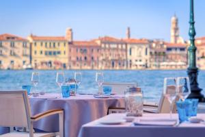 een tafel met wijnglazen en stoelen met uitzicht op het water bij Hilton Molino Stucky Venice in Venetië