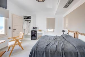 a white bedroom with a bed and a chair at NOS Suites in Ermoupoli