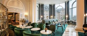 un restaurante con sillas verdes, mesas y ventanas en Hilton Brussels Grand Place en Bruselas