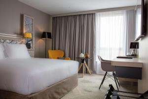 Habitación de hotel con cama blanca grande y escritorio. en Hilton Garden Inn Paris Massy, en Massy