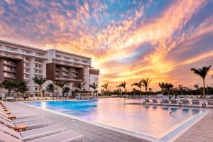una piscina en un complejo con sillas y una puesta de sol en Embassy Suites By Hilton Aruba Beach Resort en Palm-Eagle Beach