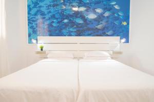 Una cama blanca en una habitación con una pintura de pescado en Alojamiento Guayarmina, en La Restinga