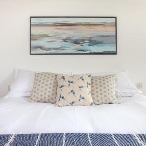 a painting hangs above a white bed with pillows at Beautiful Rural Cottage by the Coast in East Portlemouth