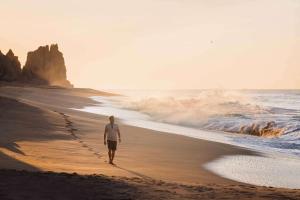 um homem andando na praia perto do oceano em Waldorf Astoria Los Cabos Pedregal em Cabo San Lucas