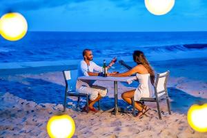 Ein Mann und eine Frau sitzen an einem Tisch am Strand in der Unterkunft PLAYA Villa in Sanctuary Resort - 100m from Private Beach - New 2023 in Hồ Tràm