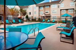 einen Pool mit Stühlen, einem Tisch und einem Sonnenschirm in der Unterkunft Residence Inn by Marriott New Orleans Metairie in Metairie