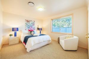 een slaapkamer met een wit bed en een witte stoel bij White Sands, 14 Whitesands Road - Pet Friendly, Linen & Air Con in Fingal Bay