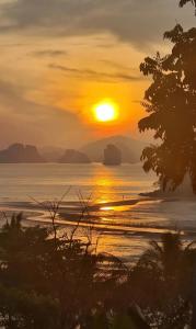 a sunset on the beach with the sun setting over the ocean at Hillhouse - Koh Yao Noi in Ko Yao Noi