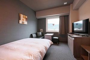中野市にあるホテルルートインGrand中野小布施のベッドとテレビが備わるホテルルームです。