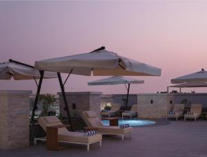 DoubleTree by Hilton Muscat Qurum في مسقط: مجموعة من الكراسي والمظلات بجانب المسبح