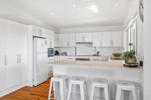 a white kitchen with white cabinets and white stools at Salt Water in Mollymook