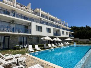 a hotel with a swimming pool and chairs and a building at Вила Quiet Bay in Sozopol