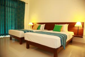 Samwill Holiday Resort في كاتاراغاما: سريرين في غرفة الفندق مع ستائر خضراء