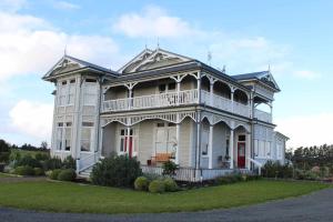 ein großes weißes Haus mit einem Balkon auf einer Wiese in der Unterkunft The Suite - Huntly House in Auckland
