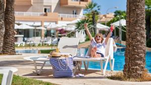 a woman is sitting in a chair by the pool at Hotel Illot Suites in Cala Ratjada