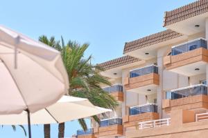 a building with a white umbrella and a palm tree at Hotel Illot Suites in Cala Ratjada