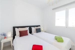 2 bedden in een witte slaapkamer met rode en groene kussens bij Casa Lolalo - Modern Villa with pool, 15min walk to Marina Rubicón in Playa Blanca