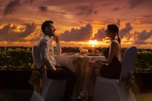 Ein Mann und eine Frau sitzen an einem Tisch vor einem Sonnenuntergang. in der Unterkunft The Trans Resort Bali in Seminyak