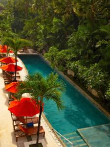 a swimming pool with red umbrellas and a palm tree at Anantara Vacation Club Legian in Legian