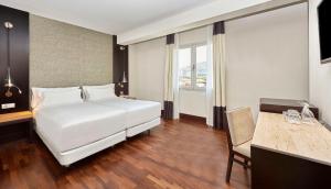um quarto de hotel com uma cama branca e uma secretária em NH Barcelona Stadium em Barcelona