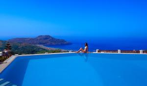 a woman sitting on the edge of a swimming pool overlooking the ocean at Stefanos Village Hotel in Plakias