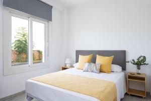 a white bedroom with a large bed with yellow pillows at Apartamentos LA PELUSA in Málaga