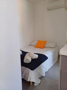 un piccolo letto in una camera bianca con un cuscino arancione di סטודיו עידן a Tel Aviv