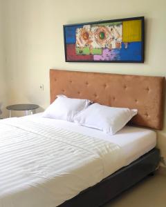 a bed with white pillows and a painting on the wall at Olivia SOHO Guest House in Legian