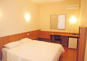 a bedroom with a bed and a desk and a window at Bernal Hotel Econômico in Ituiutaba