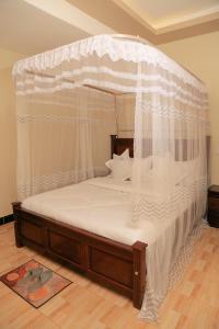 uma cama de dossel com cortinas brancas e piso em madeira em Scindia Suites hotel em Jinja