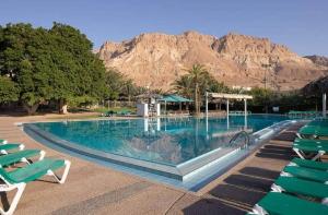 uma grande piscina com cadeiras verdes e uma montanha em Zehava's Zimmer em Ein Gedi