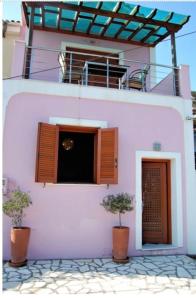 um edifício cor-de-rosa com dois vasos de árvores à sua frente em Odysseos St. Loft em Vathi