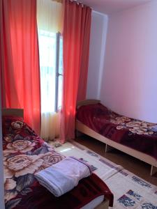 Коттедж Иссык-Куль солнышко VIP 2 في Chok-Tal: غرفة نوم بسريرين ونافذة ذات ستائر حمراء