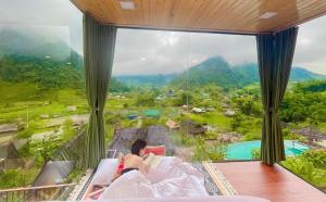 a couple sitting in a bed in a room with a large window at Mường Lống Ecogarden 