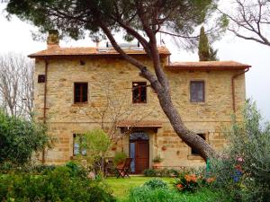 una vieja casa de piedra con un árbol delante en La Mulattiera, en Scarlino