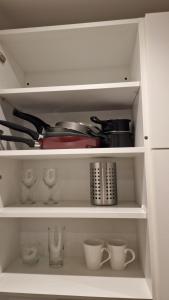 un armario blanco con tazas y utensilios. en London Stadium Apartment en Londres