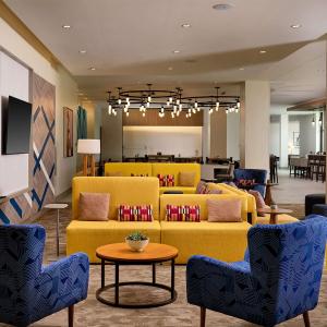 eine Lobby mit gelben Sofas, einem Tisch und Stühlen in der Unterkunft Hilton Garden Inn Grapevine At Silverlake Crossing, Tx in Grapevine