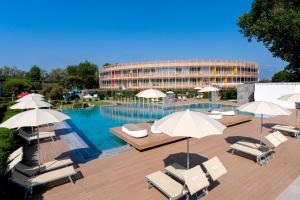 ein Pool mit Stühlen und Sonnenschirmen sowie ein Gebäude in der Unterkunft Isola di Albarella Hotel Capo Nord in Isola Albarella