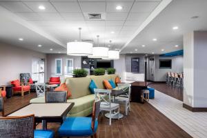 a waiting room with a couch and tables and chairs at Home2 Suites by Hilton Charlotte University Research Park in Charlotte