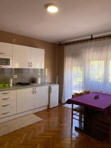 une cuisine avec des placards blancs et une table avec une table violette dans l'établissement Apartman Lavanda, à Drvar