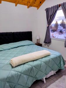 a bed with a green comforter and a window at Cabaña Maca Tobiano in El Calafate